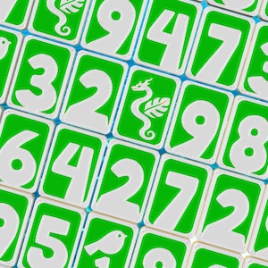 May include: Close-up of a collection of green and white number tiles. Each tile features a large white number against a green background. Some tiles have small white illustrations of a bird or a seahorse. The tiles are arranged in a grid pattern.