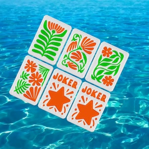 May include: Six playing cards with floral designs in orange and green, and two cards with orange starbursts and the word "JOKER". The cards are set against a backdrop of blue water.