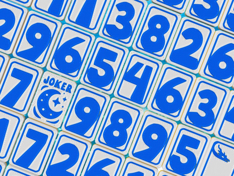 May include: Close-up of a game tile set with blue numbers and a "JOKER" card. The tiles have a white background with blue borders and numbers. The "JOKER" card features a moon and star design.