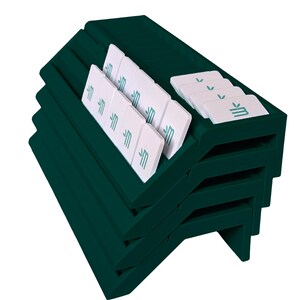 May include: A dark green tiered display rack featuring multiple angled slots. Several rectangular white tiles are arranged within the slots, each printed with a teal logo consisting of a stylized letter M and two small leaves above it.
