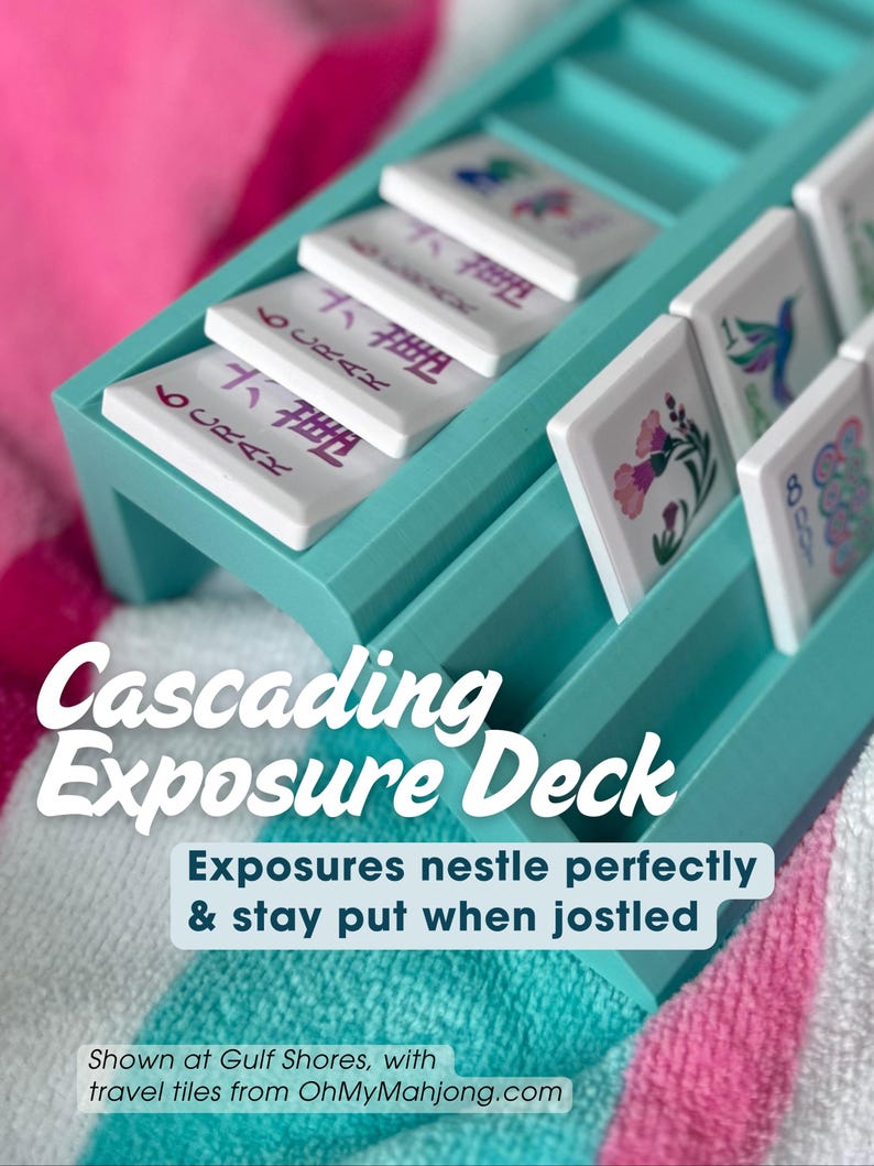 May include: A teal plastic cascading exposure deck rack for mahjong tiles. The rack features tiered slots holding white tiles with colorful floral and numerical designs. Text on the image reads: Cascading Exposure Deck, Exposures nestle perfectly & stay put when jostled, Shown at Gulf Shores, with travel tiles from OhMyMahjong.com.