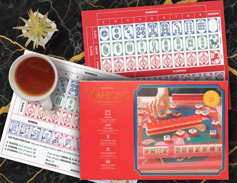 May include: A red Mahjong game set with a gold-colored title and a detailed illustration of the game in progress. The set includes tiles, a game board, and instructions. A cup of tea and a small plant are also visible.