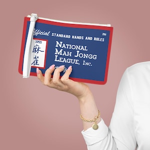May include: A rectangular clutch with a blue background and red trim, featuring the text "NATIONAL MAH JONGG LEAGUE, INC." and "STANDARD HANDS AND RULES." The clutch has a white wrist strap and a zipper closure.