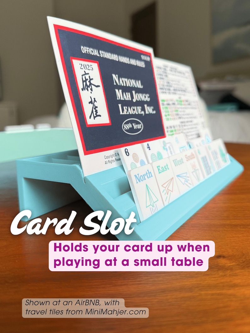 May include: A light blue plastic card holder stand designed to support a National Mah Jongg League 2025 official standard hands and rules card. The stand features a grooved slot for upright card placement, shown with game tiles.