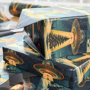 Peut inclure: Des boîtes cadeaux enveloppées dans du papier au design spatial. Le papier d'emballage présente un fond bleu foncé avec des illustrations d'OVNIs, d'arbres et d'étoiles. On aperçoit également des ciseaux et un rouleau de papier assorti.