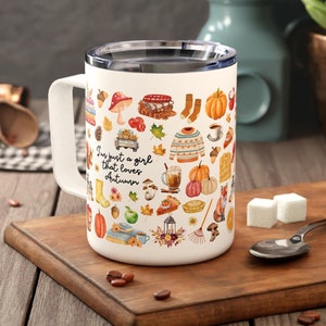 May include: White ceramic mug with a colourful autumn-themed design. The mug features a variety of fall icons, including pumpkins, leaves, acorns, and a fox. The text "I'm just a girl that loves autumn" is printed on the mug.