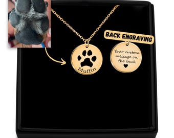 May include: Gold necklace with a paw print pendant and a smaller round pendant with the text "Your custom message on the back" and a heart. The larger pendant has the name "Muffin" engraved on it. The necklace is in a black box with a tag that says "BACK ENGRAVING".
