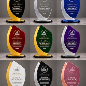 Puede incluir: Una colección de nueve premios en forma de llama con paneles acrílicos de varios colores y detalles metálicos. Cada trofeo muestra el texto Honestly Innovation, Yo remèt li bay, WIDERSON y JIVÈ 2026 impreso en blanco o negro en la superficie.