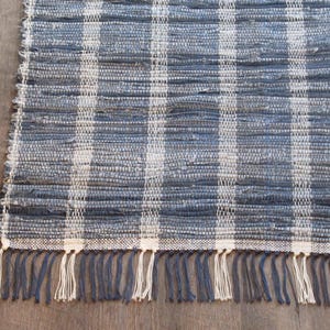 May include: A blue and white plaid rug with a fringed edge. The rug is made of woven material and has a textured appearance. The fringe is a mix of blue and white. The rug is suitable for a variety of home decor styles.