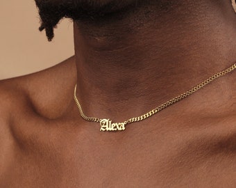 Puede incluir: Un collar de cadena dorada con un colgante de placa que dice "Alex" en fuente gótica.