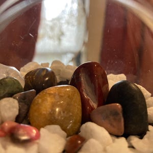 May include: A glass orb filled with white, gray, and brown stones. There are also several colorful stones, including red, orange, green, and black.