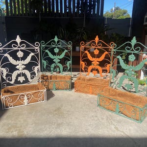 May include: Four decorative metal planters in white, green, and orange. Each planter has a rectangular coir liner and ornate scrollwork and floral designs. The planters are suitable for outdoor use and add a touch of elegance to any garden or patio.