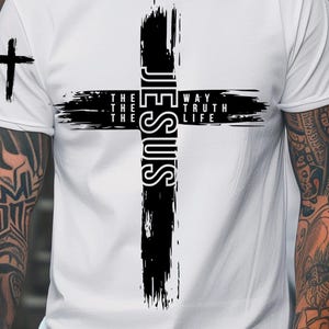 Puede incluir: Camiseta blanca con un gran diseño de cruz negra con la palabra "JESUS" verticalmente en el centro. La cruz incluye las palabras "THE WAY, THE TRUTH, THE LIFE". Una pequeña cruz está en la manga izquierda. Descarga digital.