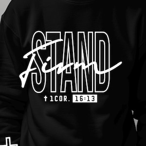 May include: Black crewneck sweatshirt with the word "STAND" in a bold, white font, with "I AM" in a cursive script overlay. The text "† 1COR. 16:13" is below. A white cross is on the left sleeve. Digital download.