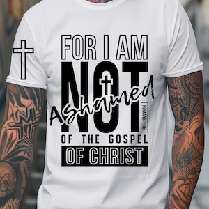 Peut inclure: T-shirt blanc avec l'inscription noire "FOR I AM NOT ASHAMED OF THE GOSPEL OF CHRIST" et une croix. La phrase "ROMANS 1:16" est également incluse. Le t-shirt a un col rond et des manches courtes.