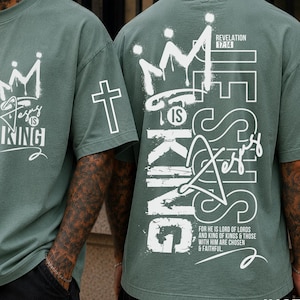 Puede incluir: Camiseta verde salvia con texto gr&aacute;fico blanco y dise&ntilde;o de corona. La parte delantera de la camiseta dice "Jes&uacute;s es Rey". La parte trasera de la camiseta presenta el texto "Jes&uacute;s es Rey" con una corona y una cruz.