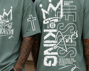 May include: Sage green t-shirt with white graphic text and a crown design. The front of the shirt reads "Jesus is King". The back of the shirt features the text "Jesus is King" with a crown and a cross.