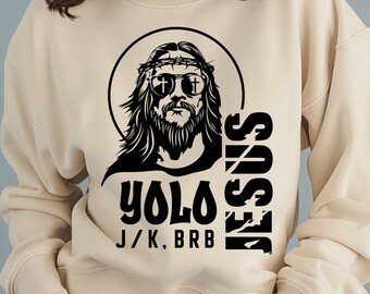 May include: A beige sweatshirt with a black graphic design of Jesus wearing sunglasses and a crown of thorns. The text "YOLO J/K, BRB JESUS" is printed vertically on the right side of the graphic.