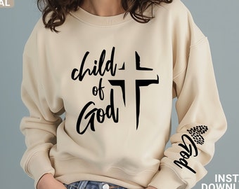 May include: A beige sweatshirt with the text "child of God" and a cross printed on the front. The text "God" is also printed on the left sleeve.