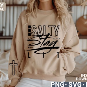 May include: A beige sweatshirt with the text "BE SALTY" in black, with "Stay Lit" in a script font. The sleeve has a black cross. The image also includes "MATT 5:13-14" and "ONLY DIGITAL DOWNLOAD".