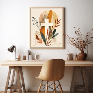 Puede incluir: Una impresi&oacute;n enmarcada con una cruz blanca rodeada de follaje abstracto en tonos naranja, marr&oacute;n y verde. El fondo es beige claro.