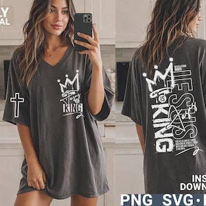 Puede incluir: Camiseta gris oscuro con cuello en V con un gr&aacute;fico de corona blanca y el texto "Jesus is King". La parte posterior de la camisa presenta un gr&aacute;fico m&aacute;s grande con el texto "He is King" y texto adicional. Una cruz blanca est&aacute; en la manga izquierda.