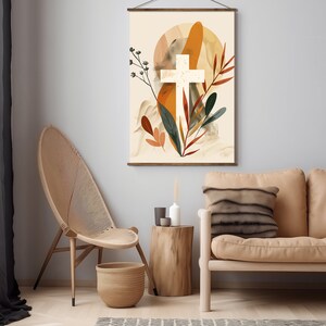 Puede incluir: Una impresi&oacute;n en lienzo beige con una cruz blanca rodeada de formas abstractas en tonos naranja, marr&oacute;n y verde. La impresi&oacute;n est&aacute; colgada en una pared gris sobre una mesa de madera y un sof&aacute; beige.