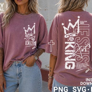Puede incluir: Una camiseta de color rosa polvoriento con el texto "Jesus is King" y un gr&aacute;fico de corona en la parte delantera. La parte posterior de la camiseta presenta el texto "Jesus is King" verticalmente, una corona y una cruz.