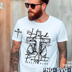May include: White t-shirt with a graphic design featuring a cross, boxing gloves, and the words "I'll Bring My Hand Fight Hallelujah." The shirt also has a small cross graphic on the sleeve.
