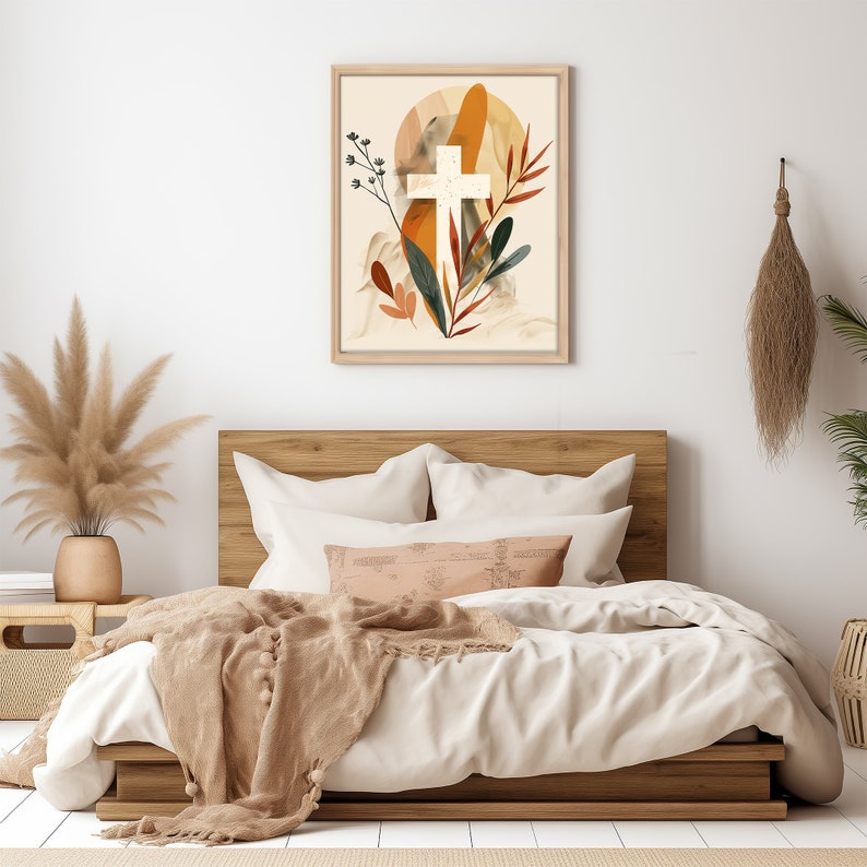 Puede incluir: Una cruz blanca con un dise&ntilde;o floral marr&oacute;n, naranja y verde sobre un fondo beige. La obra de arte est&aacute; enmarcada en un marco de madera claro y est&aacute; colgada en una pared blanca sobre una cama con un edred&oacute;n blanco y una manta de lana marr&oacute;n.