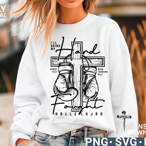 May include: White sweatshirt with a black graphic of a cross, boxing gloves, and the words "I'll bring my hand fought" and "Hallelujah." The design includes the phrases "Heart Felt" and "Been Through Hell."