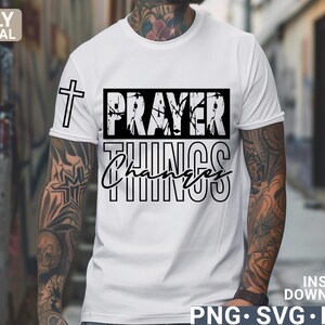Peut inclure: T-shirt blanc avec une croix noire et le texte "Prayer Changes Things" dans une police d'écriture en détresse.
