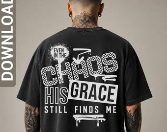 May include: A black t-shirt featuring a white graphic design on the back with the text "EVEN IN THE CHAOS HIS GRACE STILL FINDS ME." The word "CHAOS" is in a checkered pattern, and the design includes spray paint splatter and drip effects.