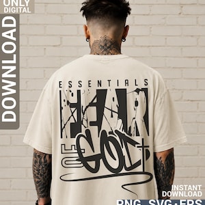 May include: A beige short-sleeved t-shirt featuring a large black graphic on the back. The design includes the text ESSENTIALS and FEAR OF GOD in a bold, distressed font with paint splatter effects and a cross symbol integrated into the lettering.