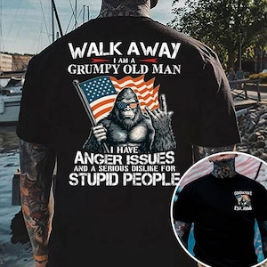May include: Black t-shirt with a graphic of a gorilla wearing sunglasses and holding an American flag. The text reads "WALK AWAY I AM A GRUMPY OLD MAN" and "I HAVE ANGER ISSUES AND A SERIOUS DISLIKE FOR STUPID PEOPLE."