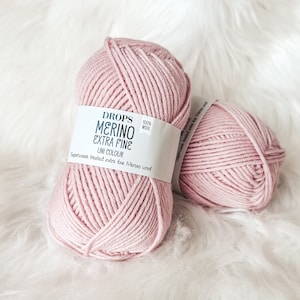 May include: Two skeins of pink Drops Merino Extra Fine yarn, 100% wool. The label reads "Drops Merino Extra Fine Uni Colour Superwash treated extra fine Merino wool."