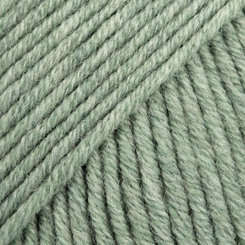 May include: Close-up of a skein of soft, green yarn. The yarn is made of wool and is perfect for knitting or crocheting.