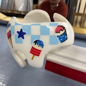 May include: A white, curved object with a blue and white checkered pattern and ice cream cone and popsicle stickers. A white and red squeegee is next to the object. The items are on a light blue surface.