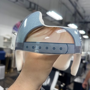 May include: A clear, molded plastic cranial helmet with a denim-patterned top section and a white interior. The helmet has a series of small, dark blue circles along the bottom edge and is designed to fit around the head.