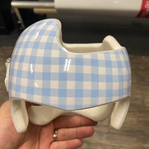May include: A white helmet with a blue and white gingham pattern. The helmet has padding around the edges.