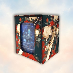May include: A rectangular deck box featuring a dark teal background with a vibrant floral pattern of red and white peonies. A long, ornate sword with a gold hilt is depicted on the side. A clear window on the front displays a trading card.