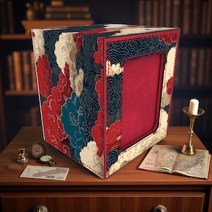 Puede incluir: Una caja decorativa con interior rojo y exterior estampado con diseños de nubes y olas rojas, blancas y azules. La caja está sobre una superficie de madera con una vela y un mapa.
