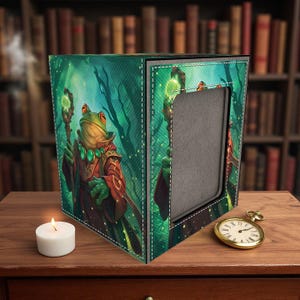Könnte beinhalten: Dekorative Box mit einem Fantasy-Frosch-Charakter in einer Waldszene. Der Frosch trägt eine rote Robe und hält einen Stab. Eine brennende Kerze und eine goldene Taschenuhr befinden sich auf der Holzoberfläche.