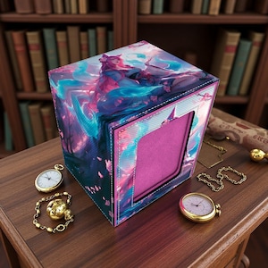 Puede incluir: Una caja decorativa con un diseño de arte de fantasía que presenta a una mujer con cabello rosado y detalles en azul. La caja tiene un interior rosa y está rodeada por un borde cosido blanco. Un reloj de bolsillo dorado, una pulsera dorada y un reloj de bolsillo dorado están sobre la superficie de madera.