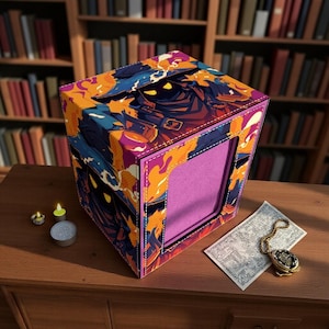 May include: A decorative box with a colorful abstract design featuring shades of blue, orange, and purple. The box has a rectangular window and is placed on a wooden surface. A pocket watch and candles are nearby.