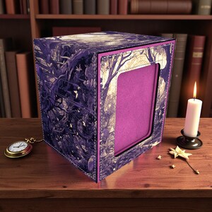 May include: A purple and black card storage box with a forest design. The box has a window with a pink interior. A gold pocket watch and a lit candle sit nearby on a wooden surface.