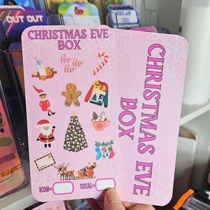 May include: Pink card with the text "Christmas Eve Box" in white letters. The card features a variety of Christmas-themed icons, including a gingerbread man, a Christmas tree, and Santa Claus. The card also has two blank spaces for "Icon" and "Total".
