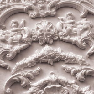 May include: A collection of white decorative mouldings featuring intricate floral and cherub designs. The pieces include various sizes and shapes, with detailed scrollwork, rosettes, and cherubic figures, suitable for home decor or craft projects.