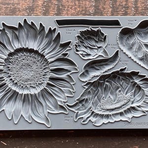 Op de afbeelding: Een grijze siliconen mal met verschillende zonnebloemontwerpen. De mal bevat een grote zonnebloem, een kleinere zonnebloem en verschillende bladeren. De mal is gelabeld met "Sunflowers IOD".