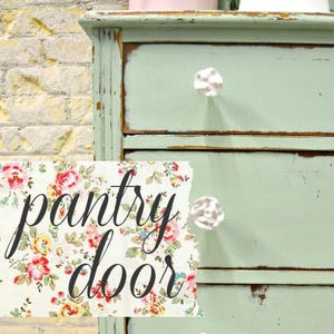 May include: A light green painted wooden dresser with two drawers and white ceramic knobs. The dresser has a distressed finish and is labeled "pantry door".